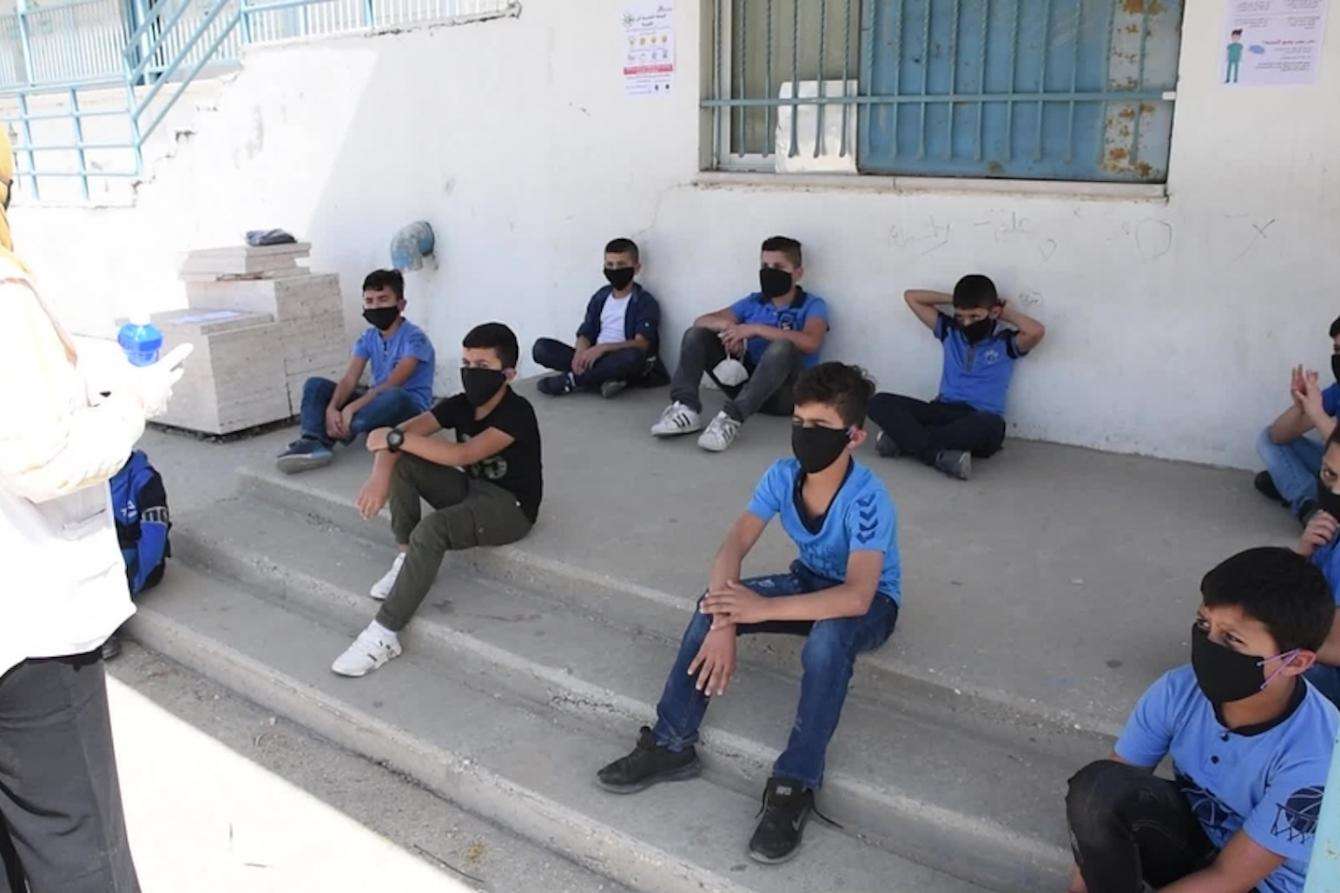 Kids sitting six feet apart on steps outside with masks on receiving instruction.